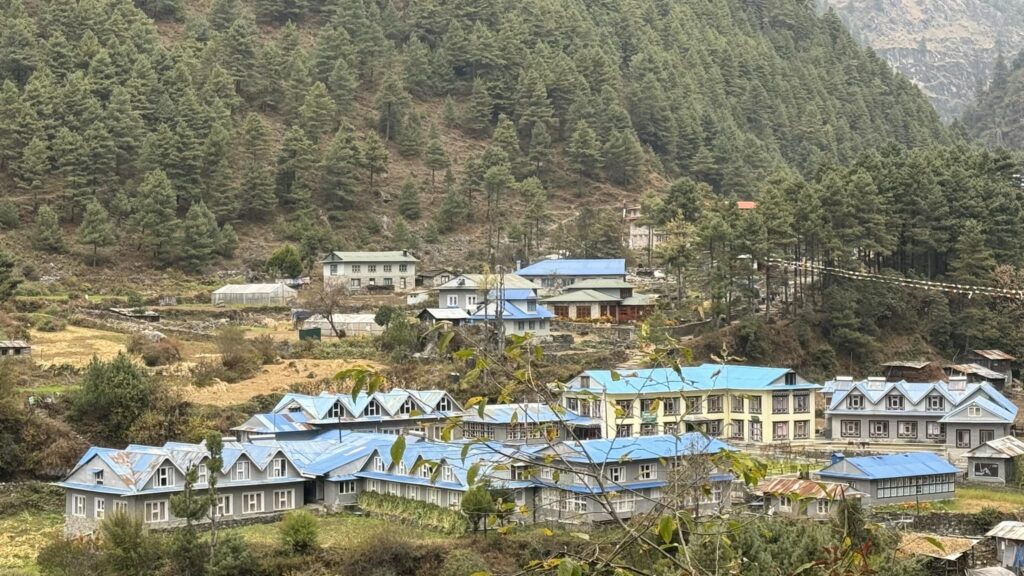 A scenic view of Phakding village with blue-roofed lodges nestled among pine-covered hills in the Everest region