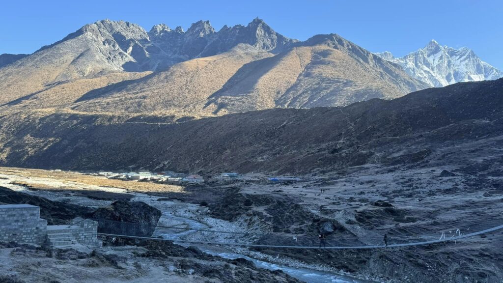 Suspension bridge with trekkers crossing a glacial stream below rugged Himalayan terrain on the way to Everest Base Camp.