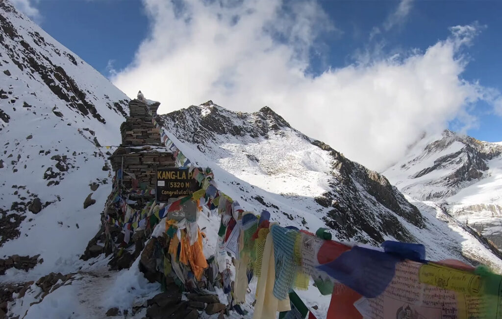 Kang La Pass at 5,320m on the Nar Phu Valley Trek with prayer flags and snowy Himalayan peaks.